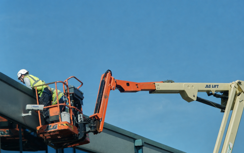 Technicien sur grue nacelle intervenant sur une toiture industrielle à accès difficiles pour l'entretien de la toiture