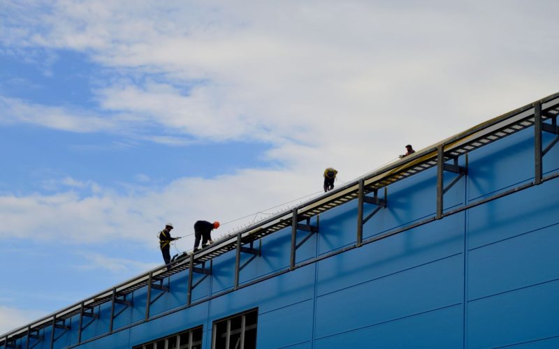 Techniciens intervenant en hauteur sur une toiture d'un hangar industriel ou logistique pour entretenir et réparer la toiture en bac acier